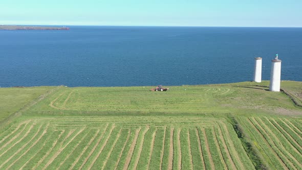 Tracking aerial dolly of red tractor in green field before blue ocean