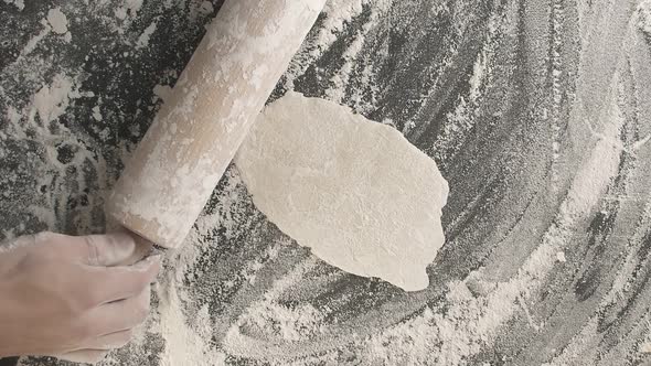 Male Hands Roll Out Baking Dough Using Rolling Pin on a Wooden Board