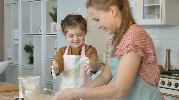 Happy Mother and Daughter Cook in the Kitchen, Daughter Laughs and Claps Her Hands and Flour Flies