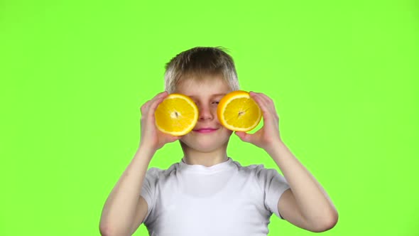 Little Boy Holds an Orange Slice and Makes Various Grimaces. Green Screen. Slow Motion