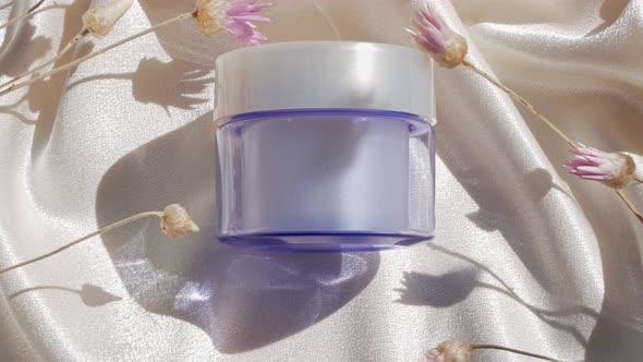 Blue glass cream jar mockup on smooth silk fabric sunlight flowers shadow water splashes Skincare 4K