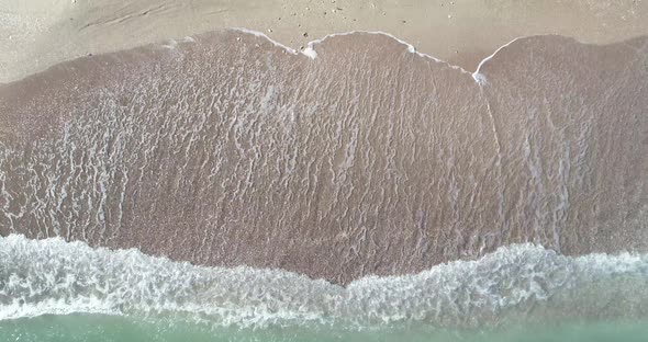 Static top down view of tropical beach, foamy ocean waves washing sand. Waves hitting sand beach