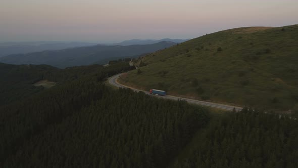 Aerial Shot of Big Cargo Truck Driving Through Foresty Hills in the Evening