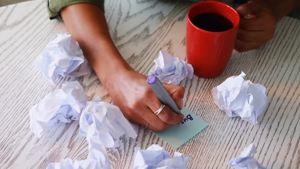 Female executive writing on sticky notes while having coffee