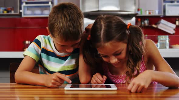 Siblings using digital tablet in kitchen