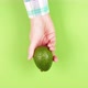 Female hand in a plaid shirt holds ripe juicy avocado hass on a green background - VideoHive Item for Sale