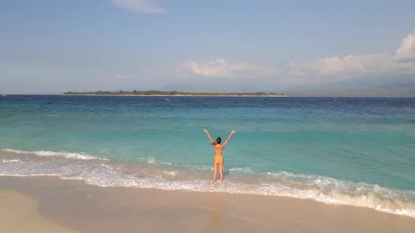Pretty young woman standing at tropical beach and raising arms up.Gili Meno Island,Indonesia.Aerial