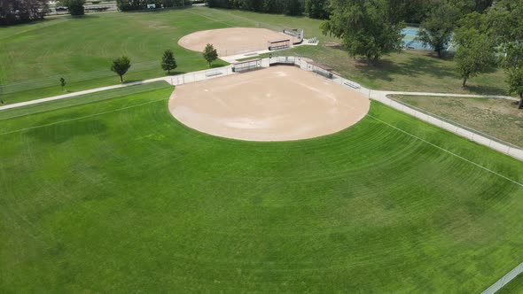 Drone view of well manicured empty ball field on a sunny day. Trees in park. Sidewalks between field