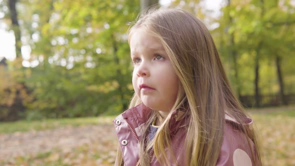 Cute Little Caucasian Girl Watches Something and Then Smiles in a Park  Closeup