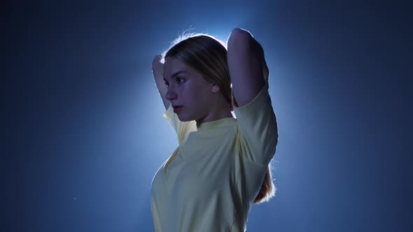 Young Woman Putting Her Hair in Ponytail Closeup Standing in Dark Studio Background with White Light