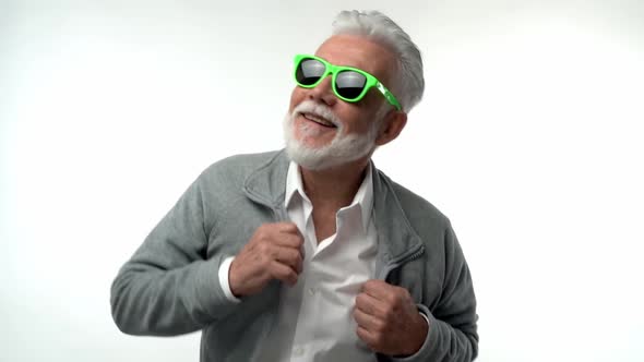 Stylish Emotional Old Man Pensioner with a Gray Beard in Green Glasses Dances with Funny Emotions on