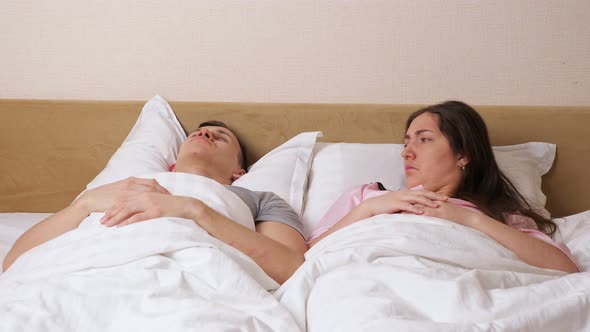 Woman Lies Near Snoring Man and Covers Ear with Pillow