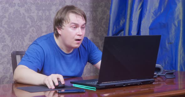 Young Man in a Blue Tshirt Enthusiastically Plays Video Game Using Laptop