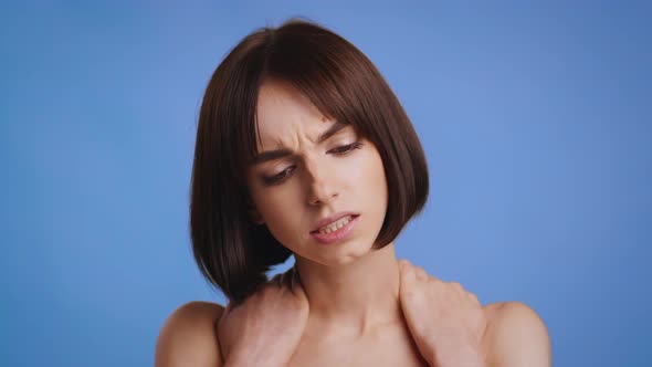 Young Woman Massaging Aching Neck Standing On Blue Studio Background