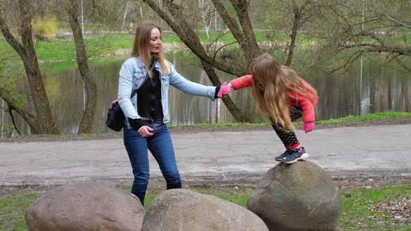 Blonde Mum Helps Young Schoolgirl Kid Jump Between Rocks