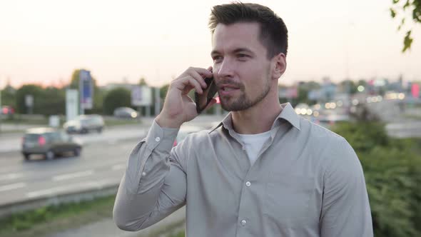 A Young Caucasian Man Talks on a Smartphone with a Smile in an Urban Area