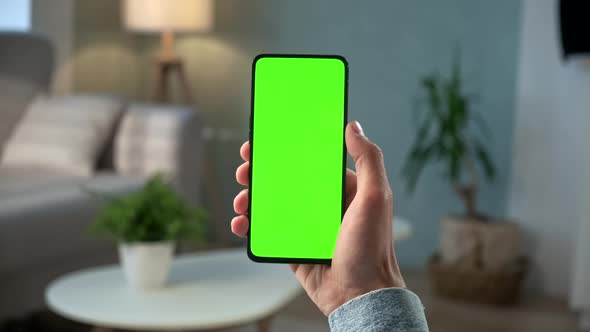 Close-up Shot of Young Man at Home Sitting on a Chair Using With Green Mock-up Screen Smartphone