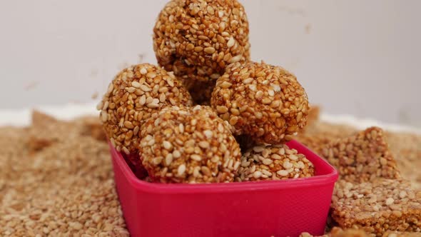 Rotating shot of plastic bowl filled with sesame seeds ladoo and sprinkling of sesame seeds