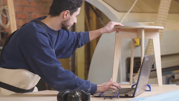 Furniture Maker Skillfully Make a Wooden Chair on Workbench and Use Laptop