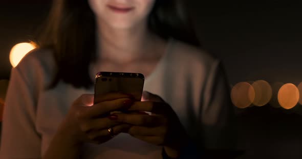 Young Girl in the Night City Writes Text Messages in a Smartphone