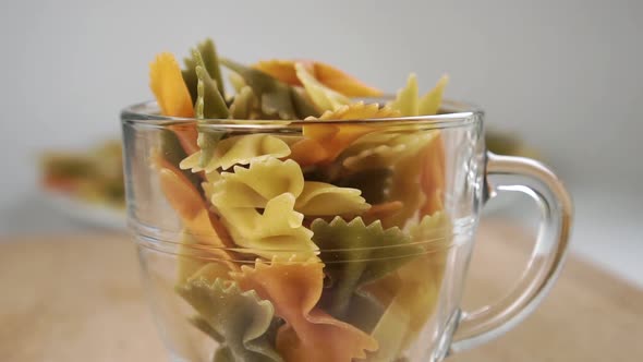 Farfalle multicolored uncooked pasta in the shape of a butterfly falls into a glass cup