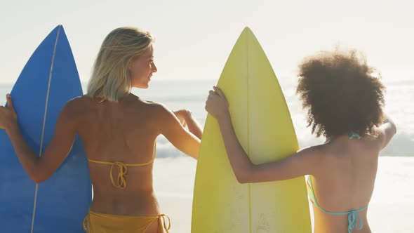 Women holding their surfboards behind the sea