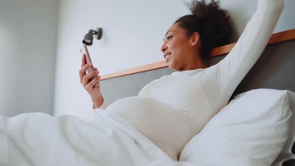 Happy African pregnant woman looking at phone