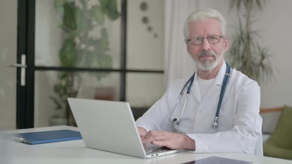 Senior Old Doctor Smiling at Camera While Using Laptop