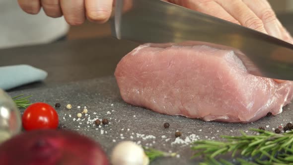 Hands Cut Pork with Knife on Background of Greens and Spices