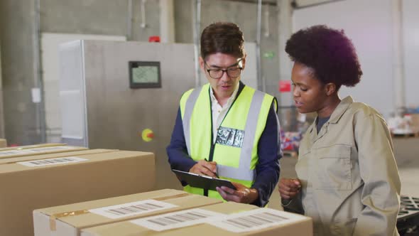 Diverse male and female workers with clipboard and boxes in warehouse