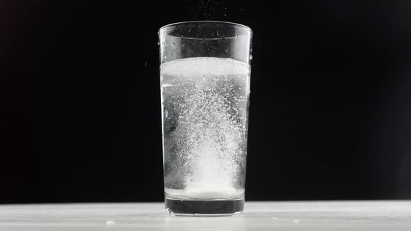 Effervescent aspirin tablet dropping to glass of water.