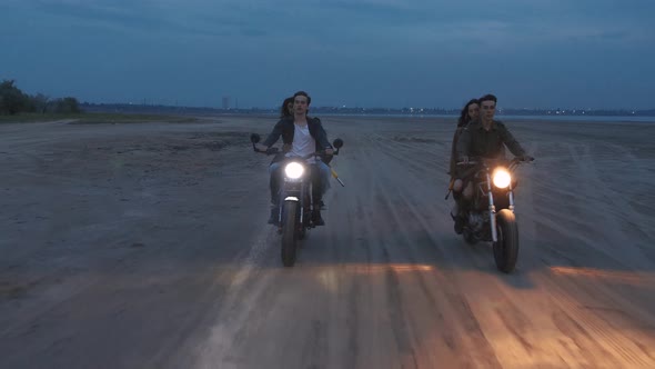 Cinematic Shot of Two Young Couples Riding on Vintage Motorcycles After Sunset on Beach Slow Motion