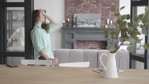 Tired Young Mother Trying To Calm Herself Standing Near the Wall with Glass of Water