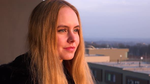 A Young Beautiful Woman Stands on a Balcony, Looks Around and Smiles at the Camera