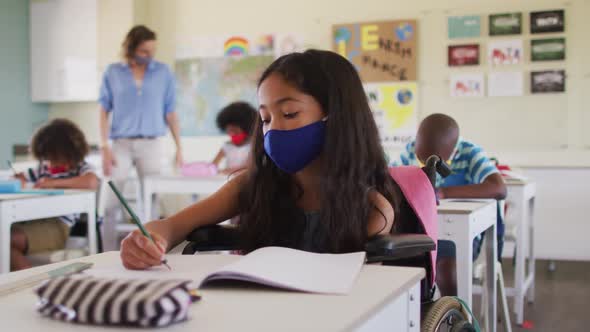 Disable girl wearing face mask writing while sitting on wheelchair in class