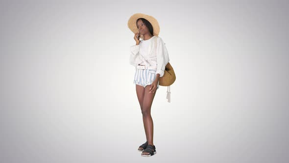 Pretty Young African American Woman in a Straw Hat Talking on Her Phone on Gradient Background.