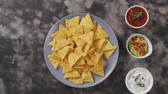 Close up of nachos in a plate and sauces on black surface