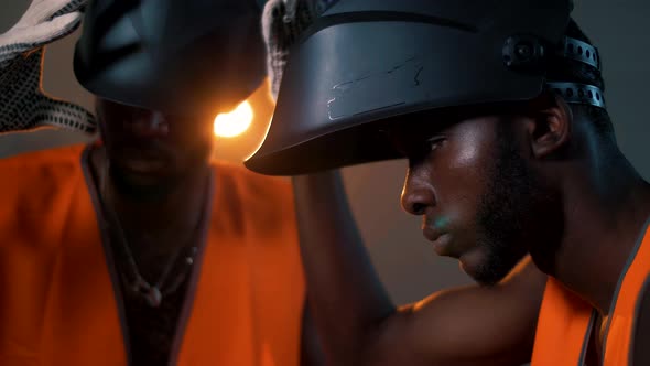 Two black workers put on welding masks before welding metal at a construction site