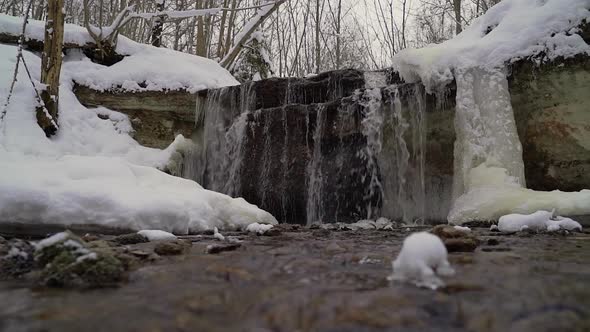 Meltwater falling over rocky frozen waterfall, winter snowy stream, cinematic