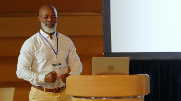 Senior African American businessman speaking on stage at podium in auditorium 4k