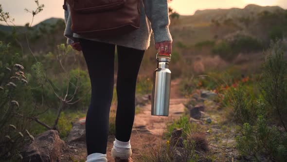 Teenager girl carrying a metal flask bottle while walking in a place full of bushes, close up tracki