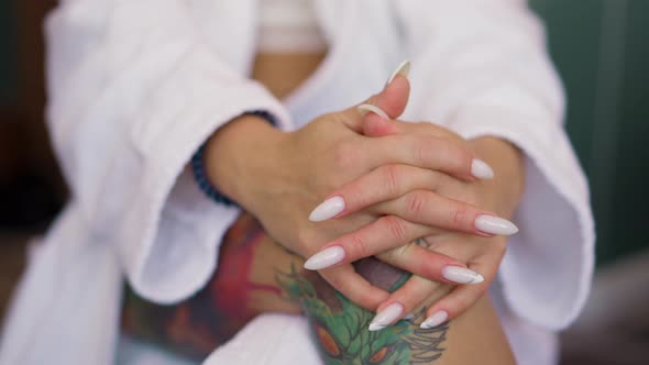 Woman with Manicure and Tattoos on Leg in Gown Sits in Room