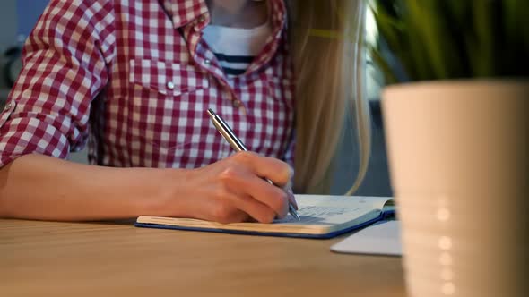 Female Writing with Pen in Notepad. Crop View of Woman with Long Blond Hair in Bright Casual Shirt