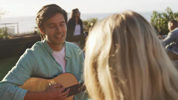 Young man playing guitar on a rooftop with his friends