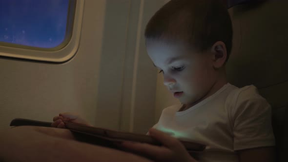 Cute Boy Traveling in an Airplane and Playing with a Computer Tablet