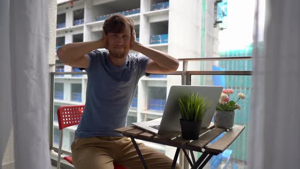 Slowmotion Shot of a Young Man Sitting on a Balcony with a Notebook and Suffering From a Loud Noise