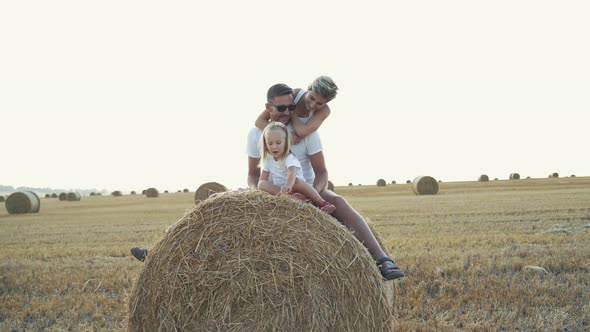 Happy Parents with Little Daughter Relaxing on a Huge Haycock in Field