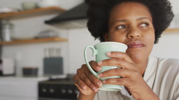 Happy african american woman drinking coffee in kitchen