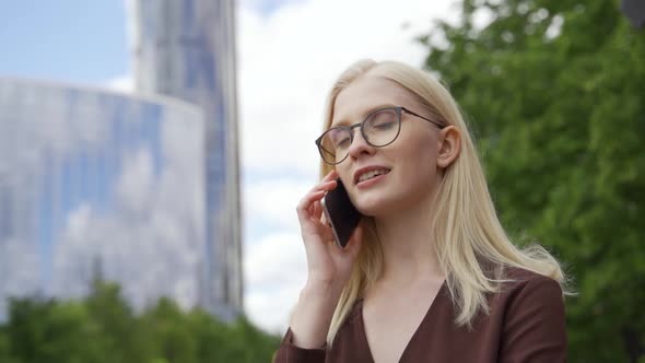 Young Business Woman Talking on the Phone Against the Backdrop of Modern Skyscrapers
