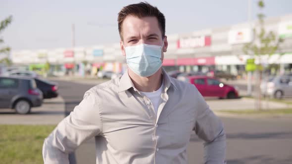 A Young Caucasian Man in a Face Mask Shows a Thumb Up to the Camera and Nods in an Urban Area